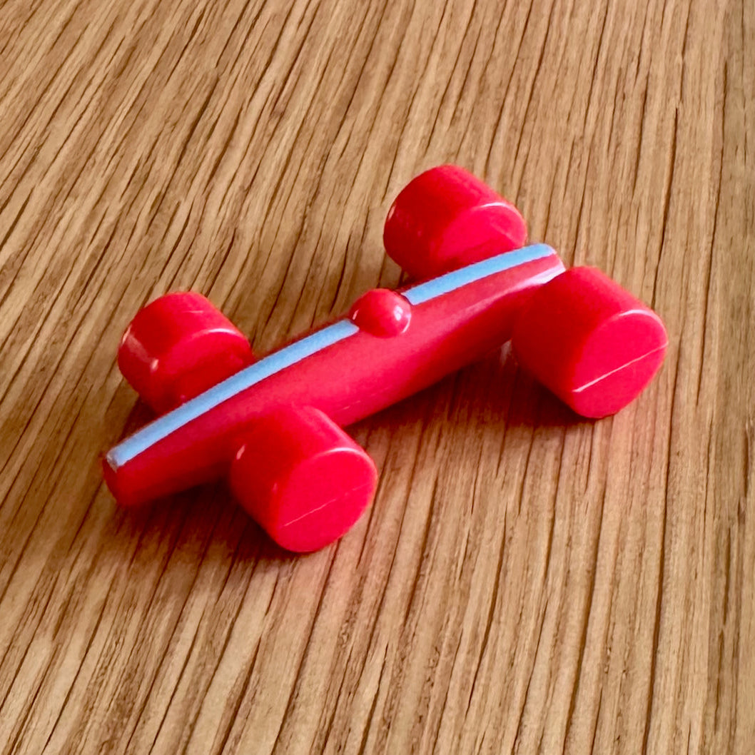 A small red plastic toy car with four wheels and a light blue center stripe, photographed on a wooden tabletop.