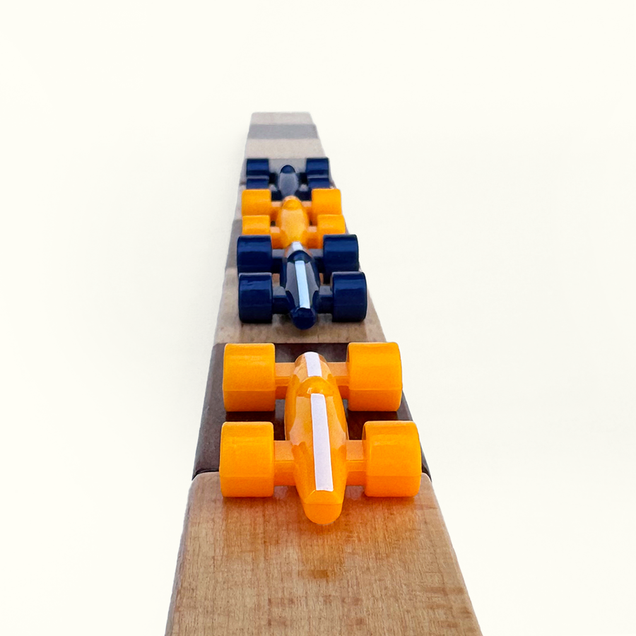 Wooden game board with orange and blue plastic race car pieces on a white background