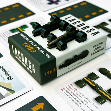 The image shows the Lacorsa 1963 Racecar Set packaging with two dark green racecars with gold stripes and several playing cards related to the 1963 Grand Prix season.