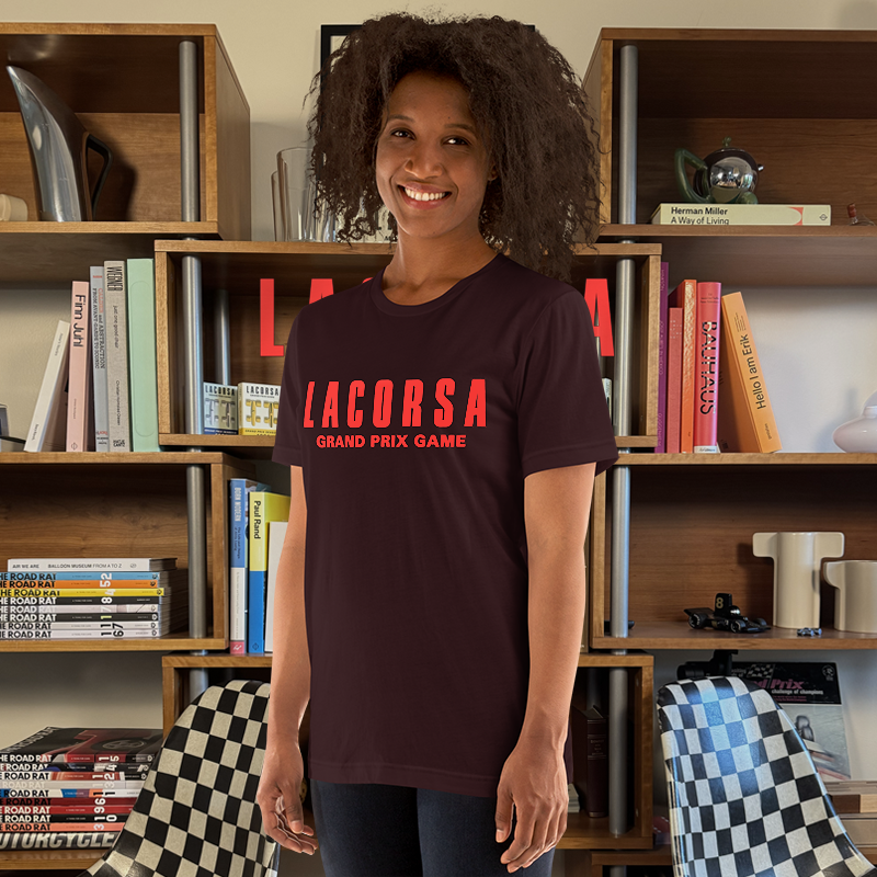 Woman wearing a dark t-shirt with 'LACORSA GRAND PRIX GAME' text in front of a bookshelf.